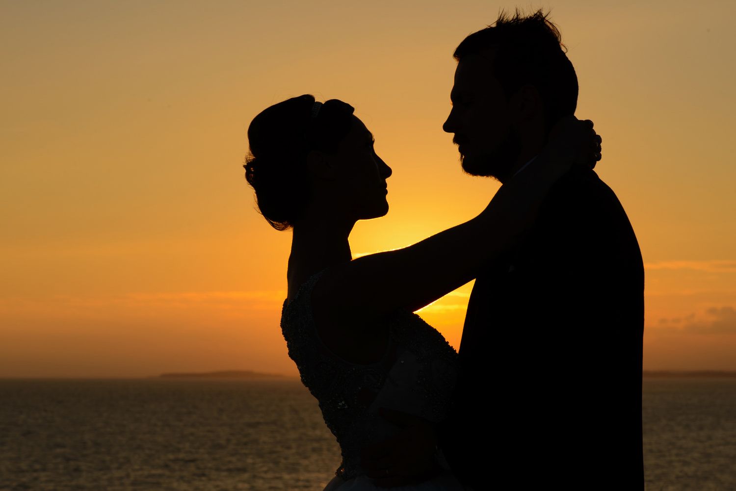 Romantic silhouette of a couple embracing at sunset over the ocean, perfect for wedding or love themes.
