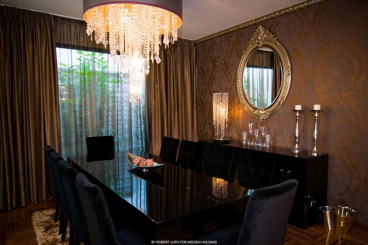 Elegant dining room with crystal chandelier, dark table, blue chairs, ornate mirror, and gold damask wallpaper.