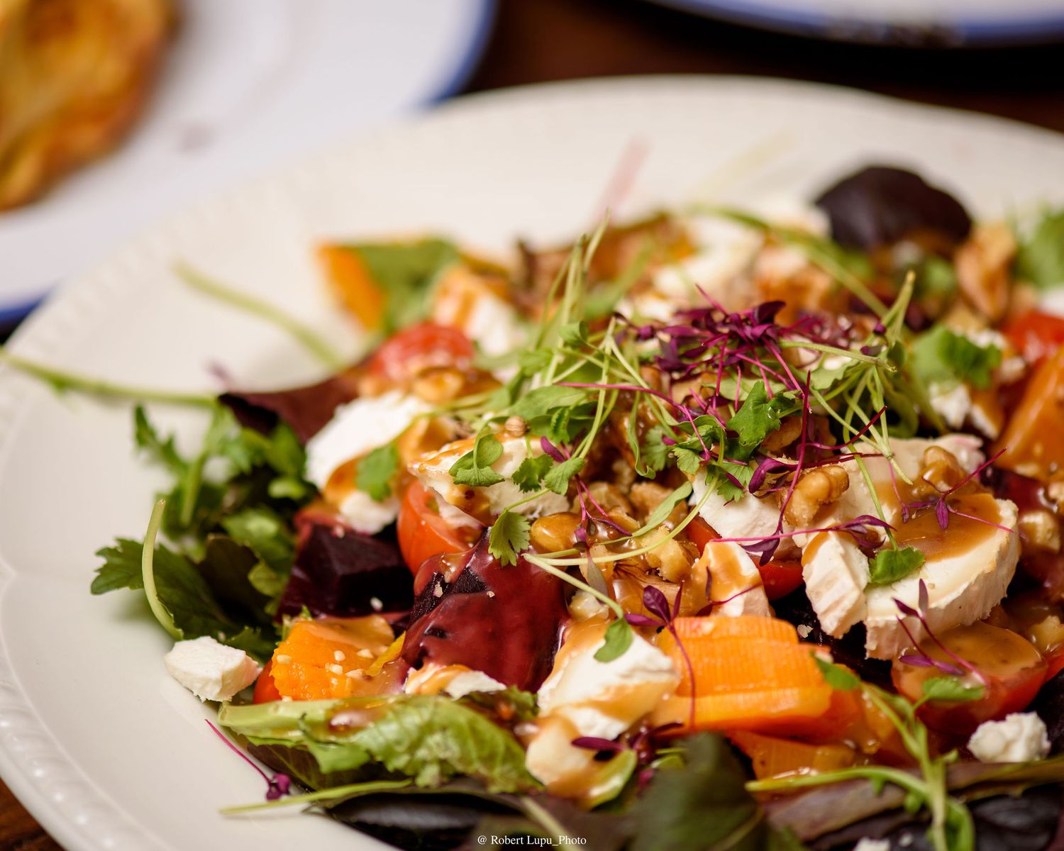 Fresh salad with arugula, roasted carrots, beets, goat cheese, and nuts on a white plate.