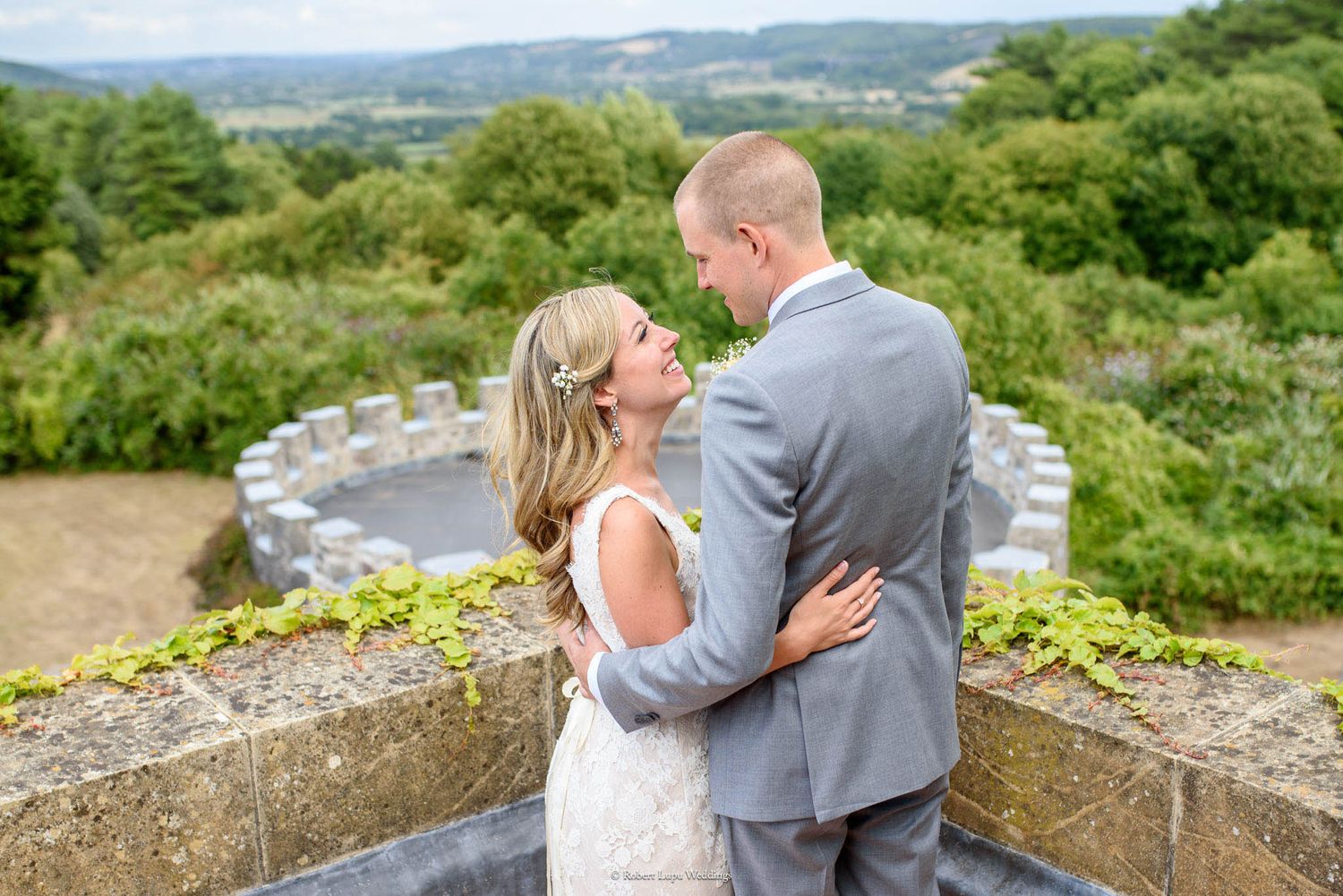 Bride and groom embracing on a stone terrace with lush green valley views at an outdoor wedding venue.