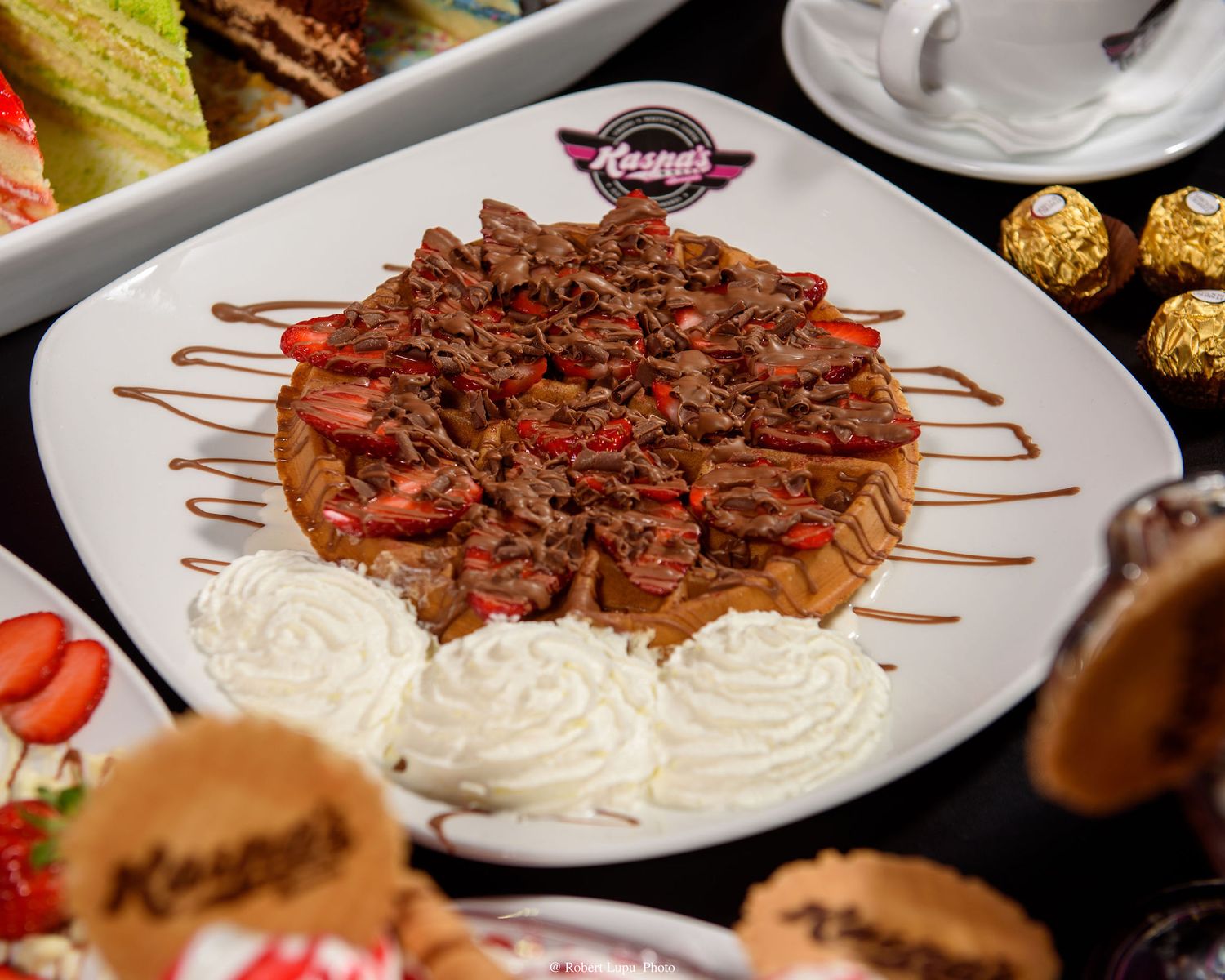 Decadent waffle topped with chocolate shavings, fresh strawberries, and whipped cream on a white plate at Kenny's.
