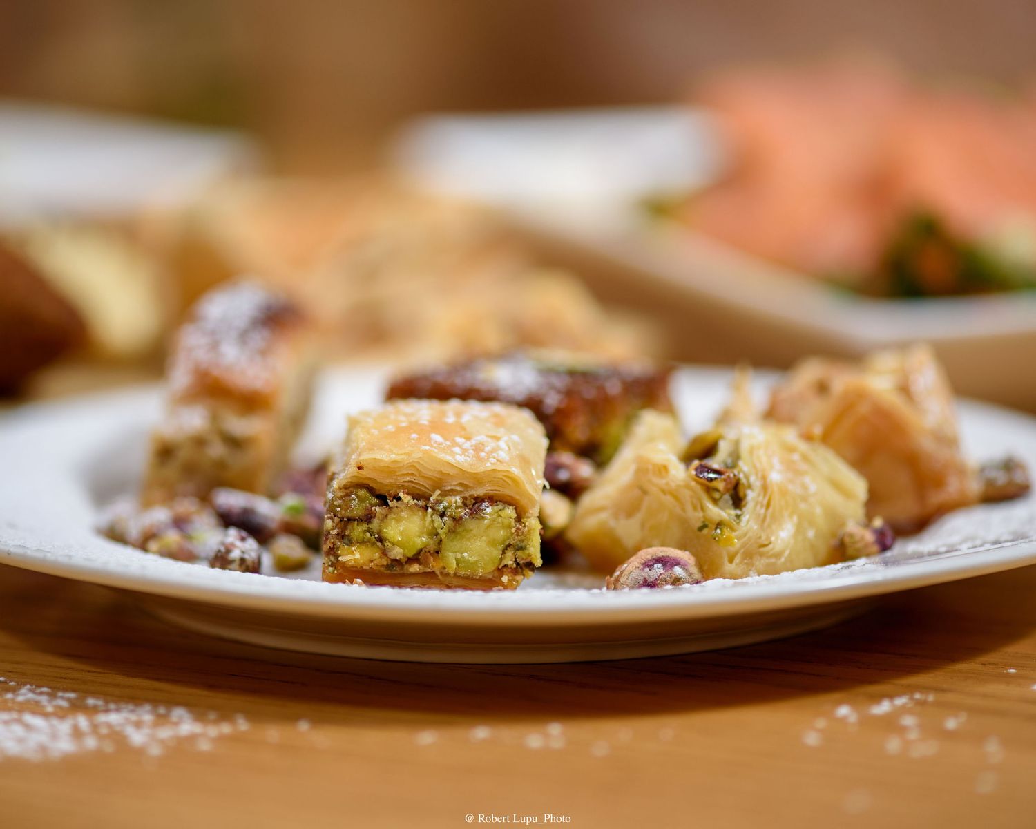 Assorted baklava pieces with pistachio filling on a white plate, dusted with powdered sugar.