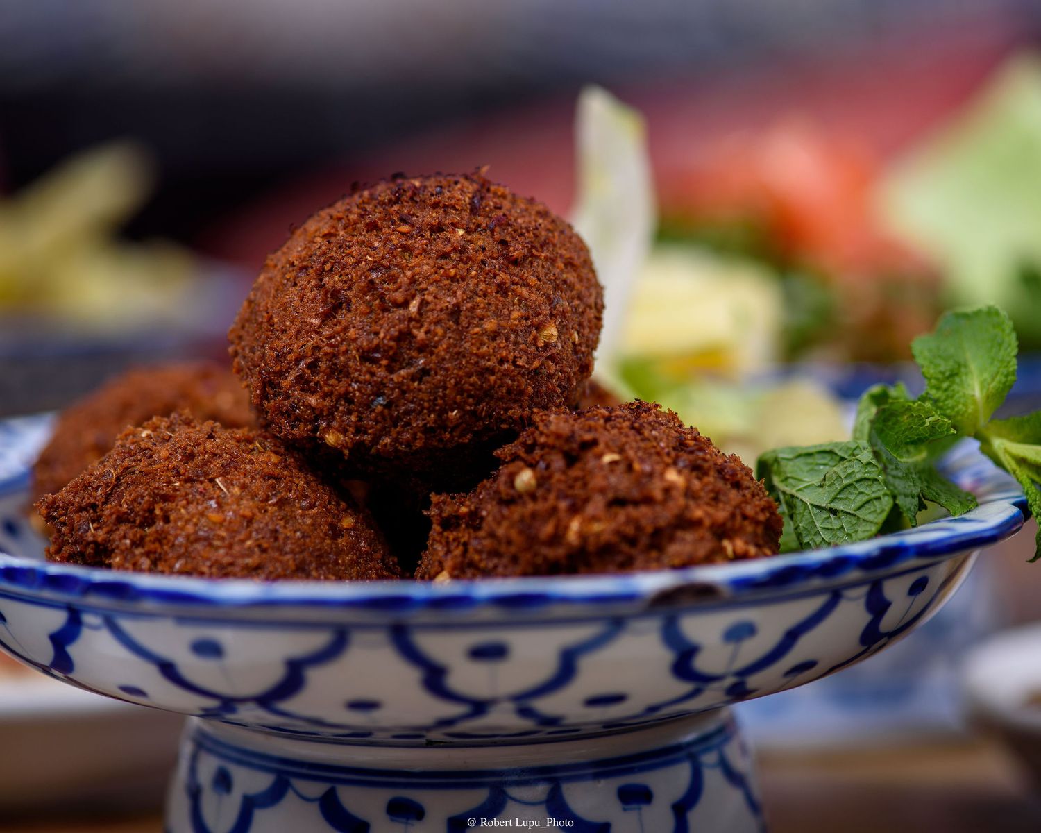 Crispy golden falafel balls served in a decorative blue and white ceramic dish with fresh mint leaves.