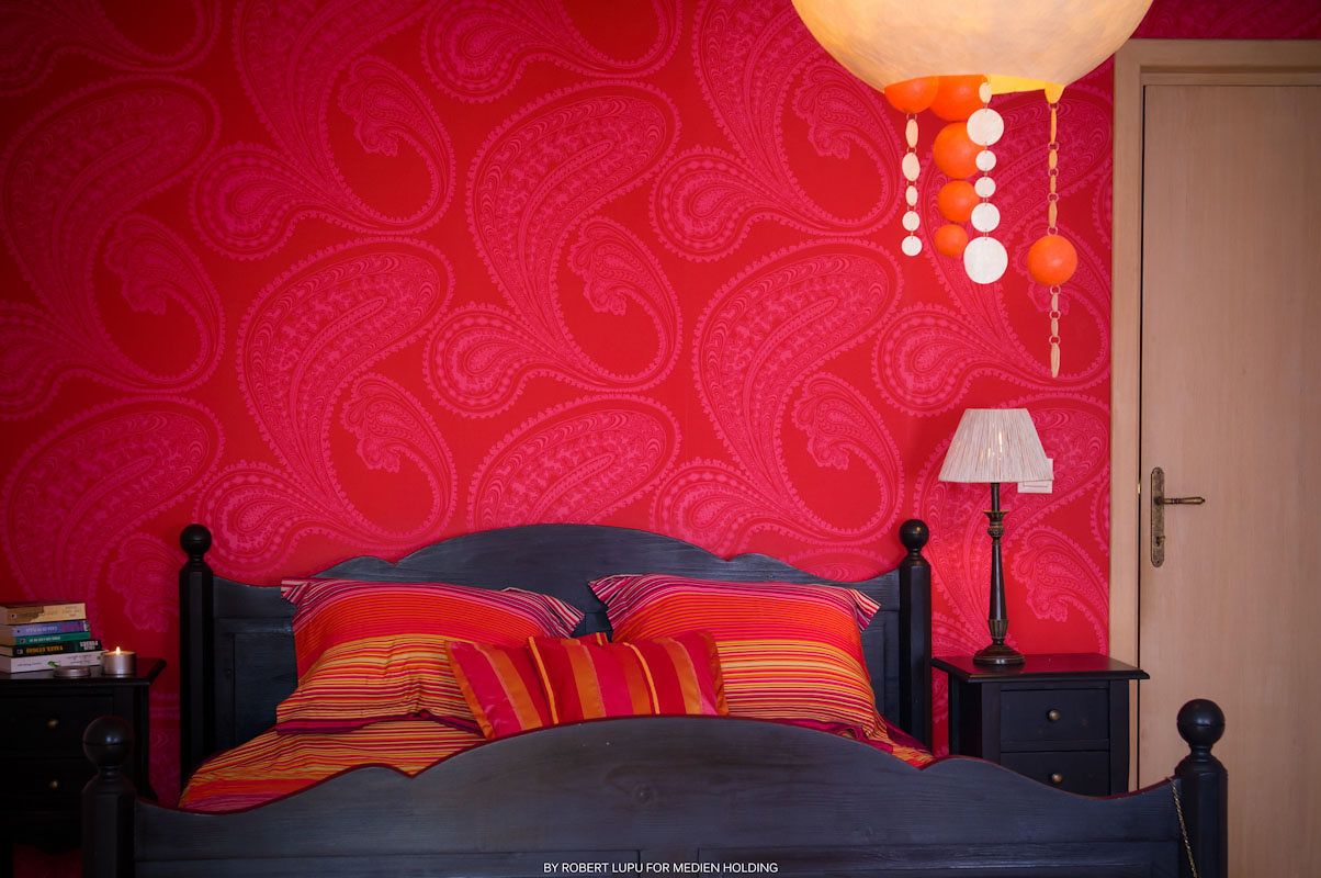 Bold red paisley bedroom wall with navy bed frame and colorful striped pillows.