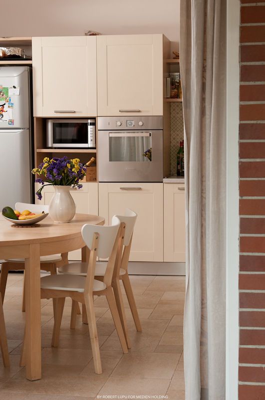 Bright kitchen with cream cabinets, round wooden table, white chairs, and fresh flowers on display.