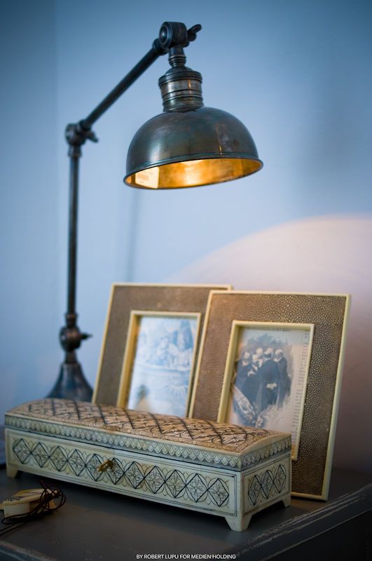 Vintage industrial desk lamp with gold interior illuminating decorative box and framed photos on a dark side table.