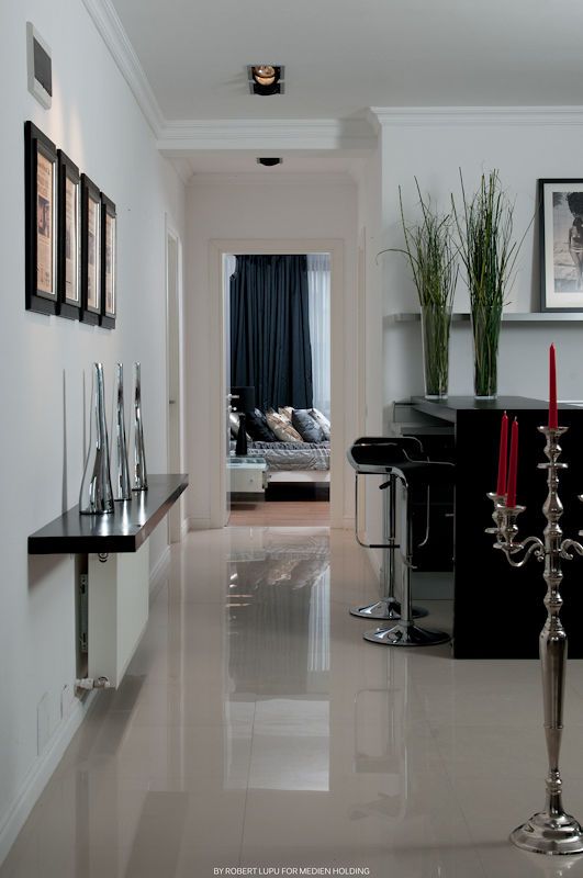 Modern hallway with glossy white floors, black bar stools, tall grass decor, framed art, and a silver candelabra in elegant interior.