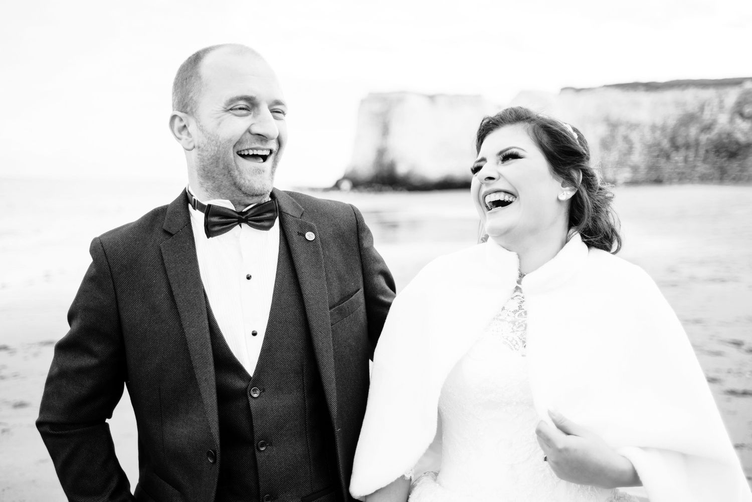 Black and white photo of laughing bride and groom outdoors on their wedding day.