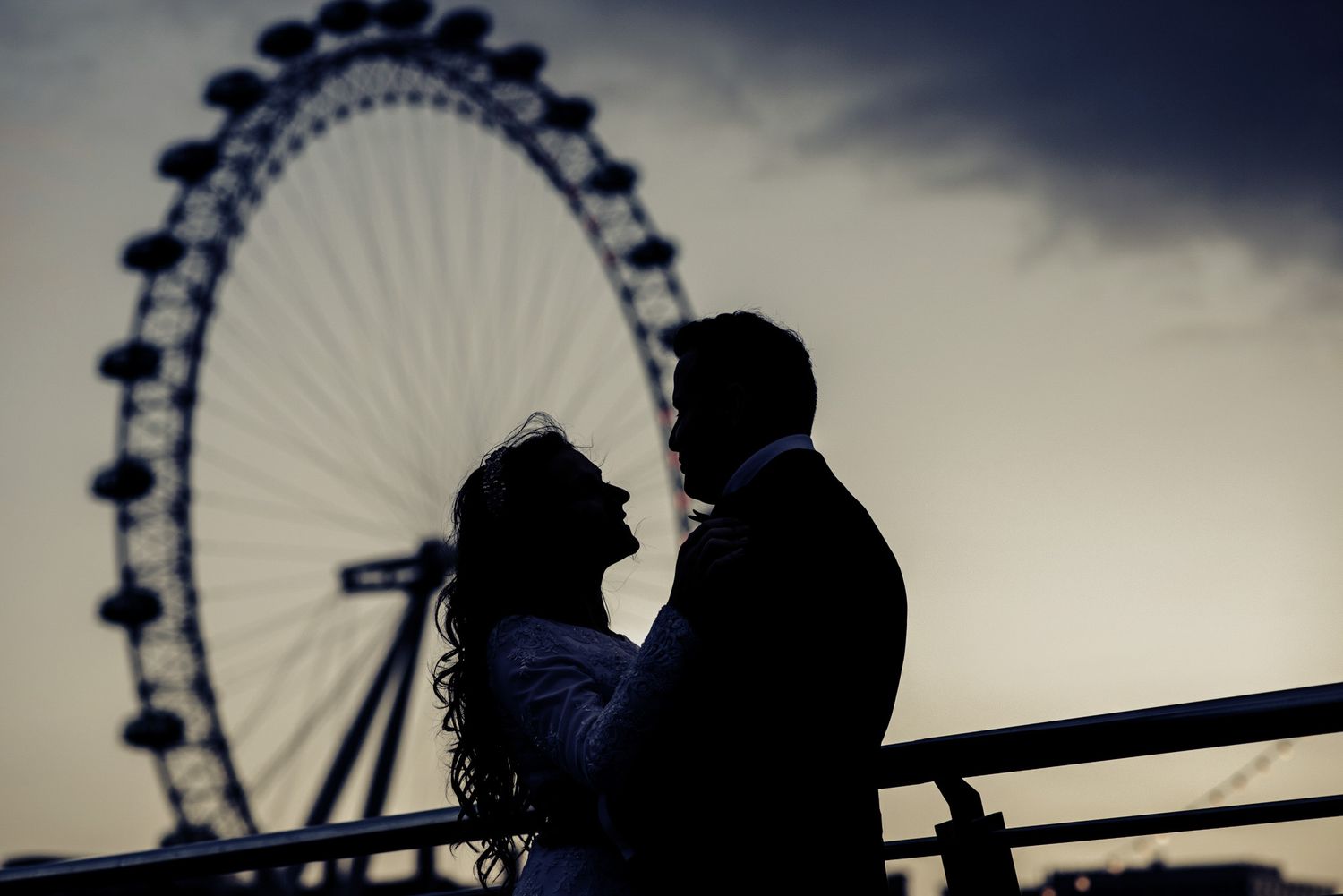 Silhouette of a bride and groom gazing at each other with the London Eye ferris wheel at sunset.
