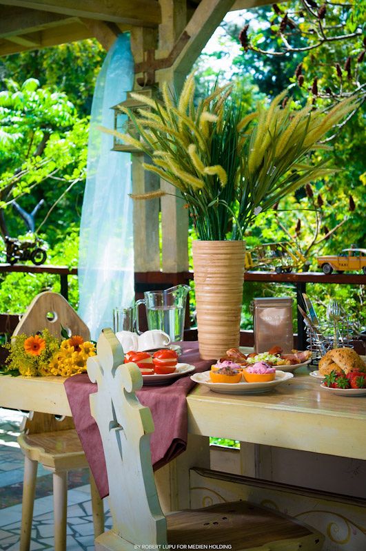 Outdoor dining table with colorful cupcakes, fresh flowers, and tall grass centerpiece on a lush garden patio.