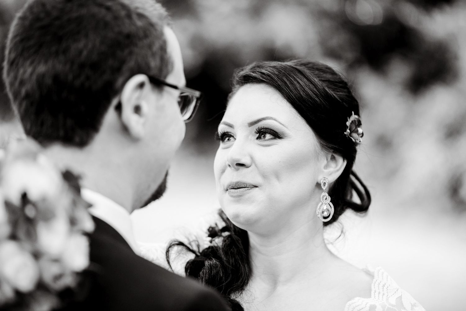Black and white wedding photo of bride gazing lovingly at groom during outdoor ceremony.