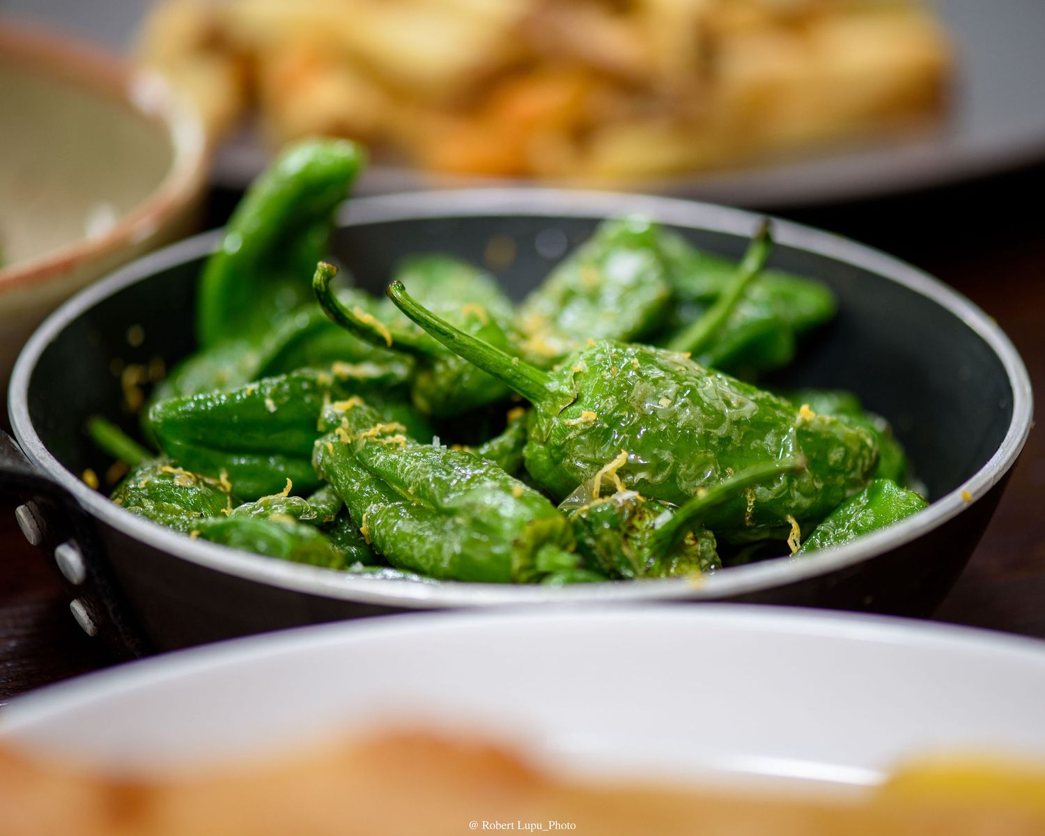 Fresh green padron peppers sautéed in a black skillet, garnished with sea salt and herbs.