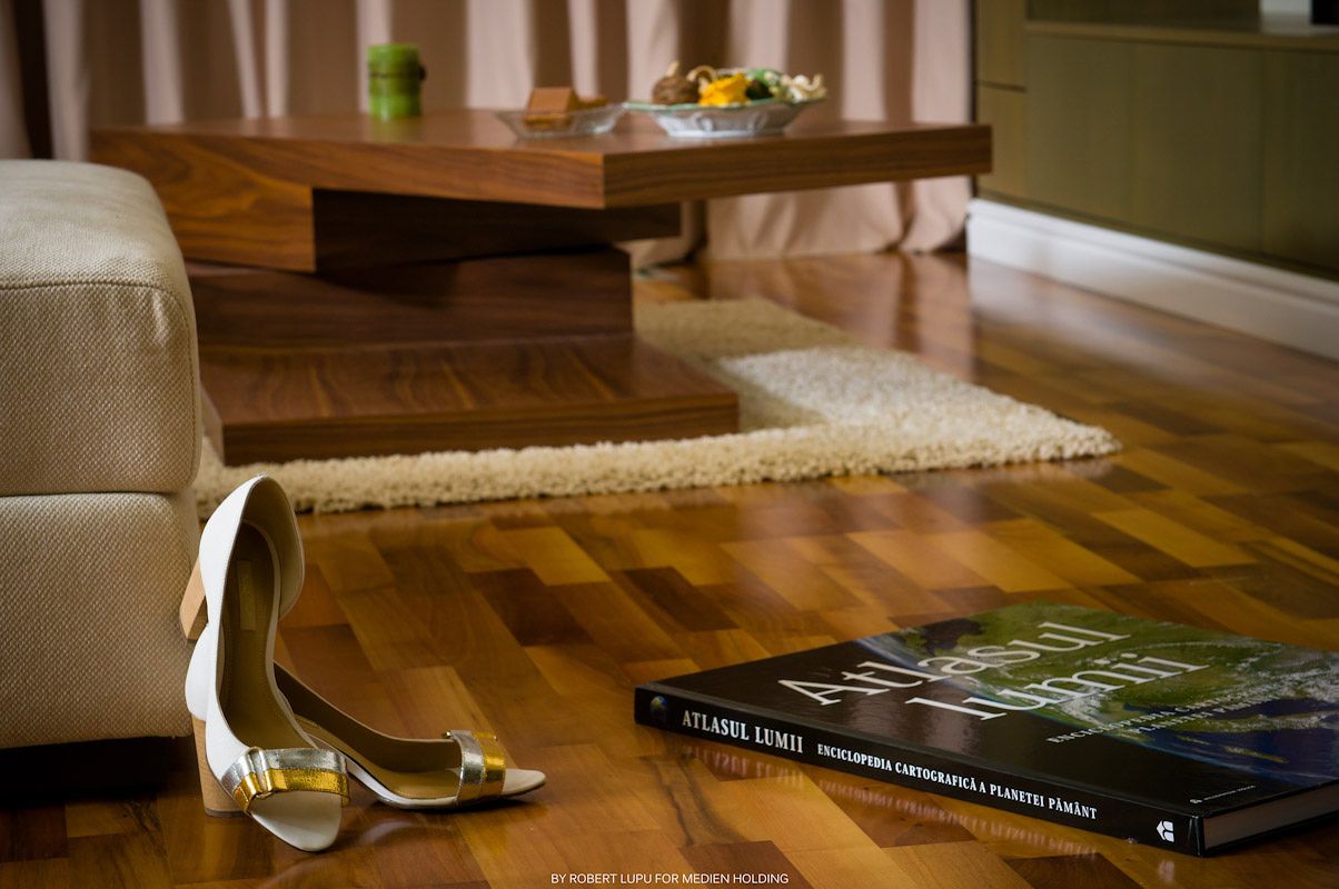 Elegant high heel shoes on hardwood floor beside a book, with a coffee table and rug in a modern living room.