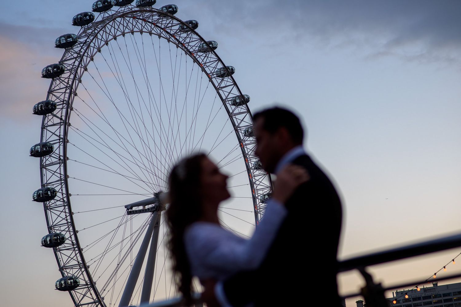 Silhouette of a couple embracing in front of the London Eye ferris wheel at dusk.