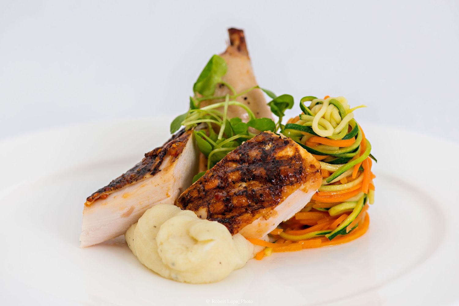 Grilled salmon fillet served with zucchini noodles, mashed potatoes, and fresh greens on a white plate.