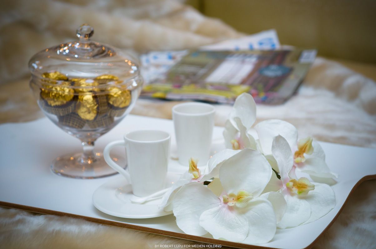 White orchid flowers beside a coffee cup and chocolate candy jar on a decorative tray.