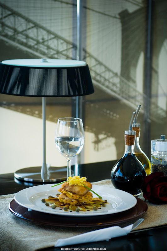 Elegant restaurant table setting with gourmet dish, wine glass, lamp, and Brooklyn Bridge view.