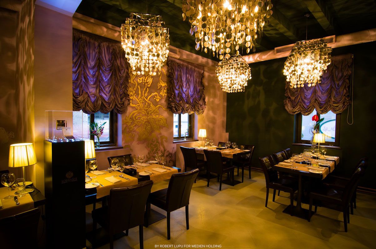 Luxurious restaurant interior with crystal chandeliers and purple drapes casting warm golden light.