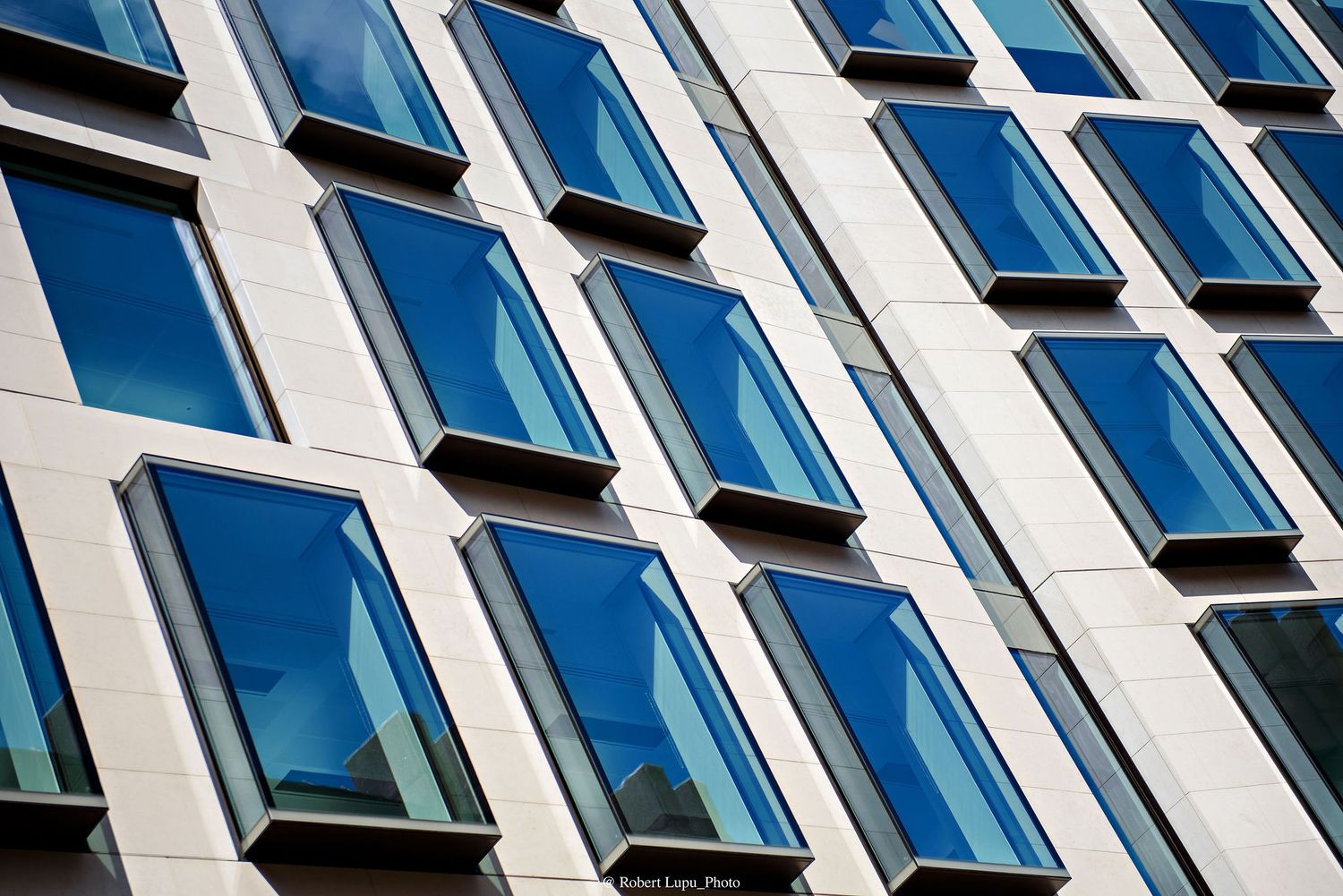 Modern office building facade featuring rows of blue reflective rectangular windows set in a light stone exterior.
