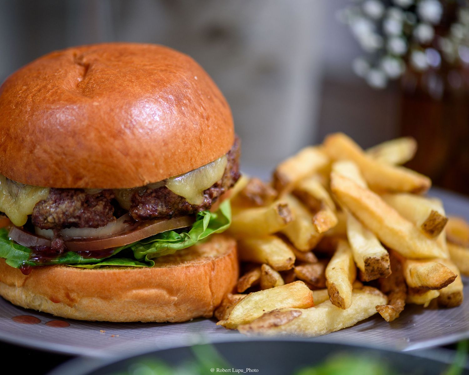 A juicy cheeseburger with lettuce and onion on a brioche bun served alongside crispy golden french fries on a plate.