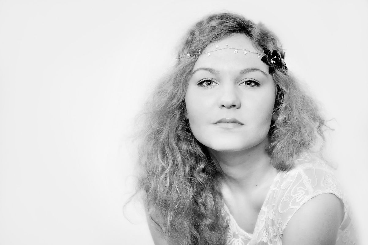 Black and white studio portrait of a young woman with curly hair and a floral hair accessory.