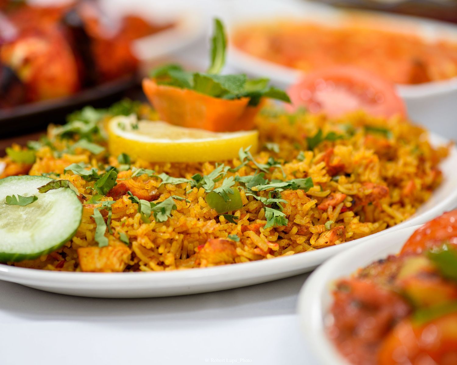 Vibrant Indian biryani rice dish garnished with lemon, cucumber, and fresh herbs on a white plate.