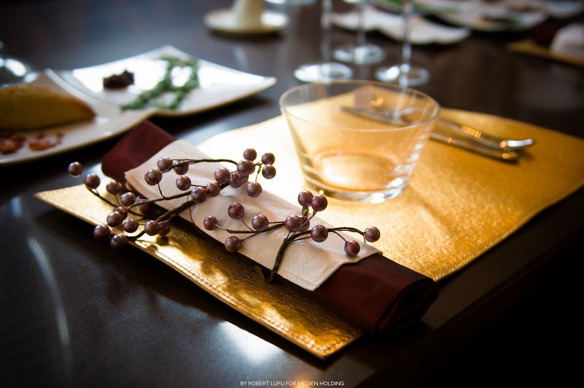 Elegant restaurant table setting with gold placemat, burgundy napkin, berry branch decor, and wine glass.