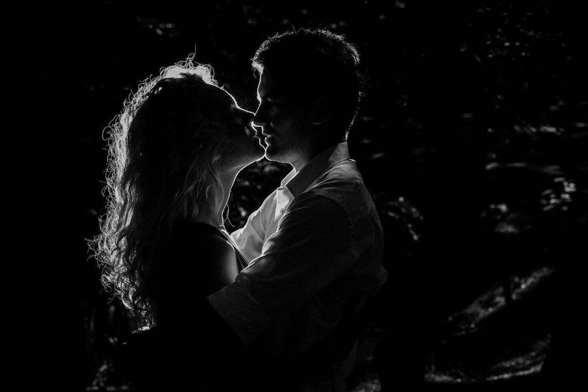 Black and white romantic silhouette of a couple embracing and about to kiss in a dark, moody setting.