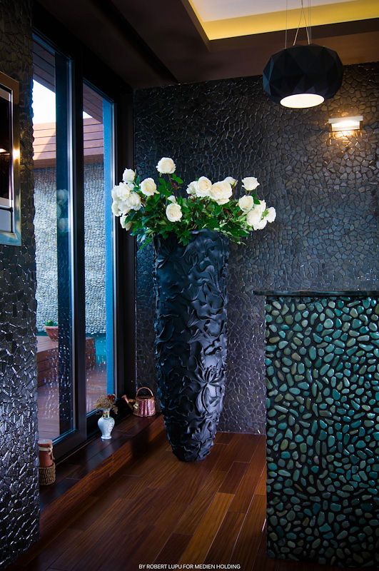 Tall dark decorative vase with white roses in modern interior with textured stone walls.