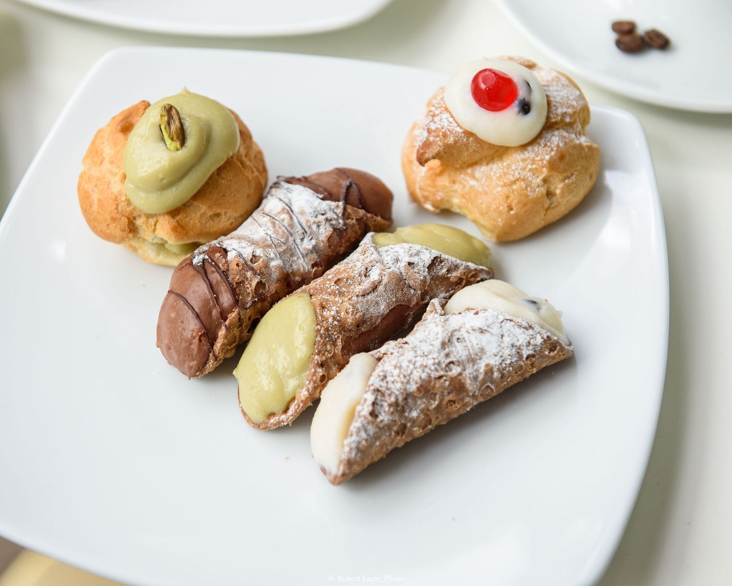 Assorted Italian pastries including cannoli dusted with powdered sugar and cream puffs on a white plate.