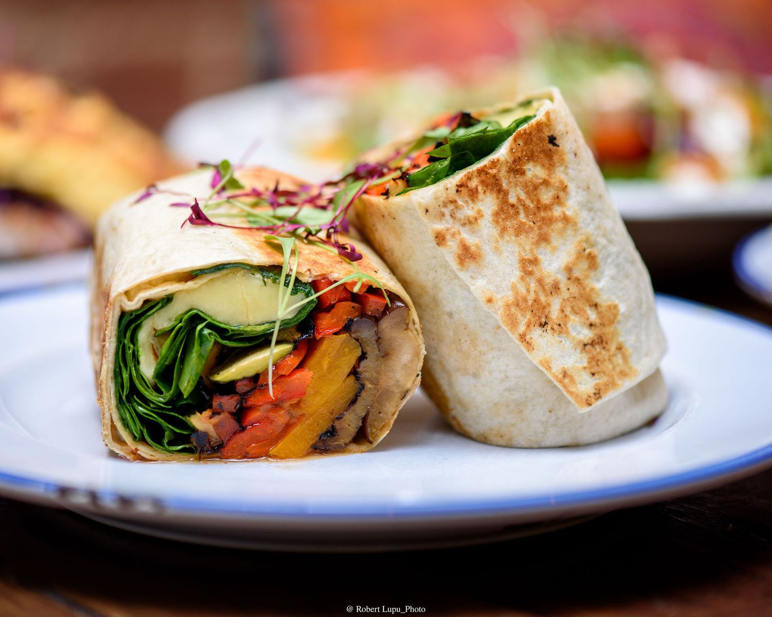Fresh vegetable wrap cut in half, filled with colorful roasted veggies and greens, served on a blue plate.