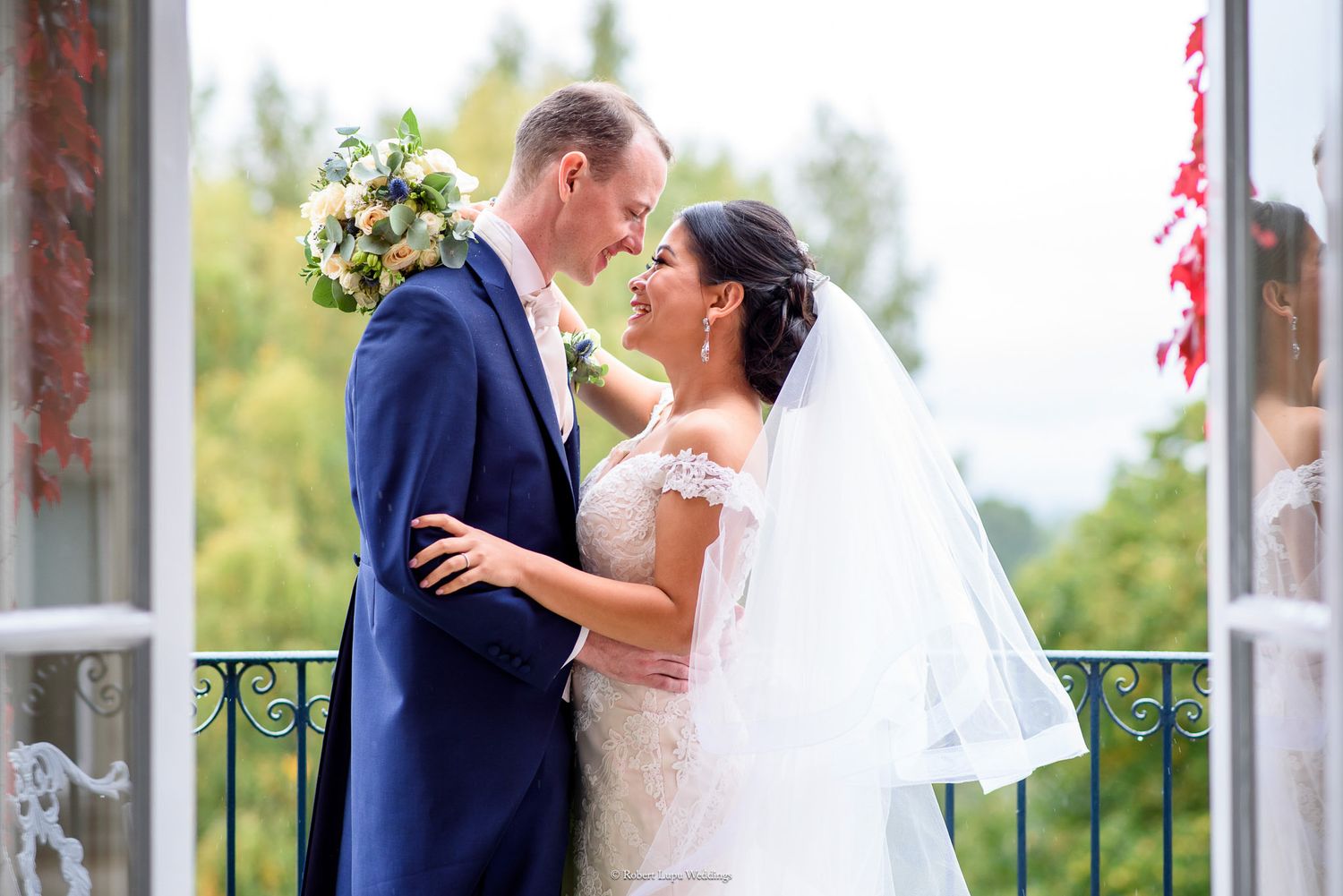 Bride and groom share a romantic moment on a balcony, with the bride holding a white bouquet on their wedding day.