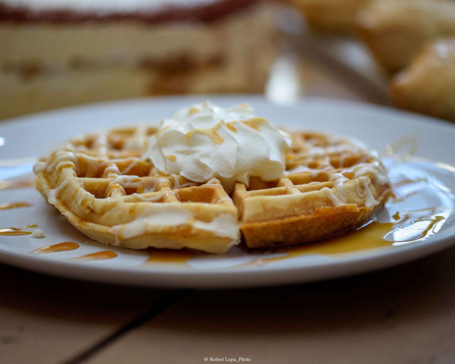 Golden waffle topped with whipped cream and maple syrup on a white plate, perfect for a classic breakfast treat.
