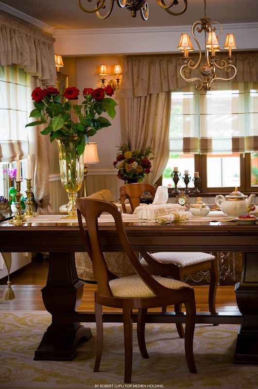 Classic dining room with dark wood table, Queen Anne chairs, red roses, chandelier, and warm ambient lighting.