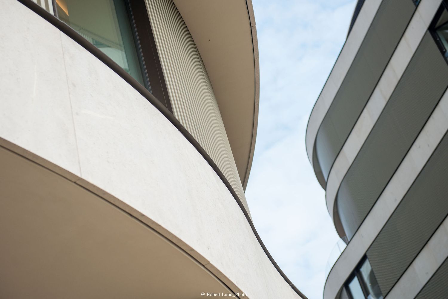 Abstract architectural detail of curved modern building facades with smooth concrete and glass against a blue sky.