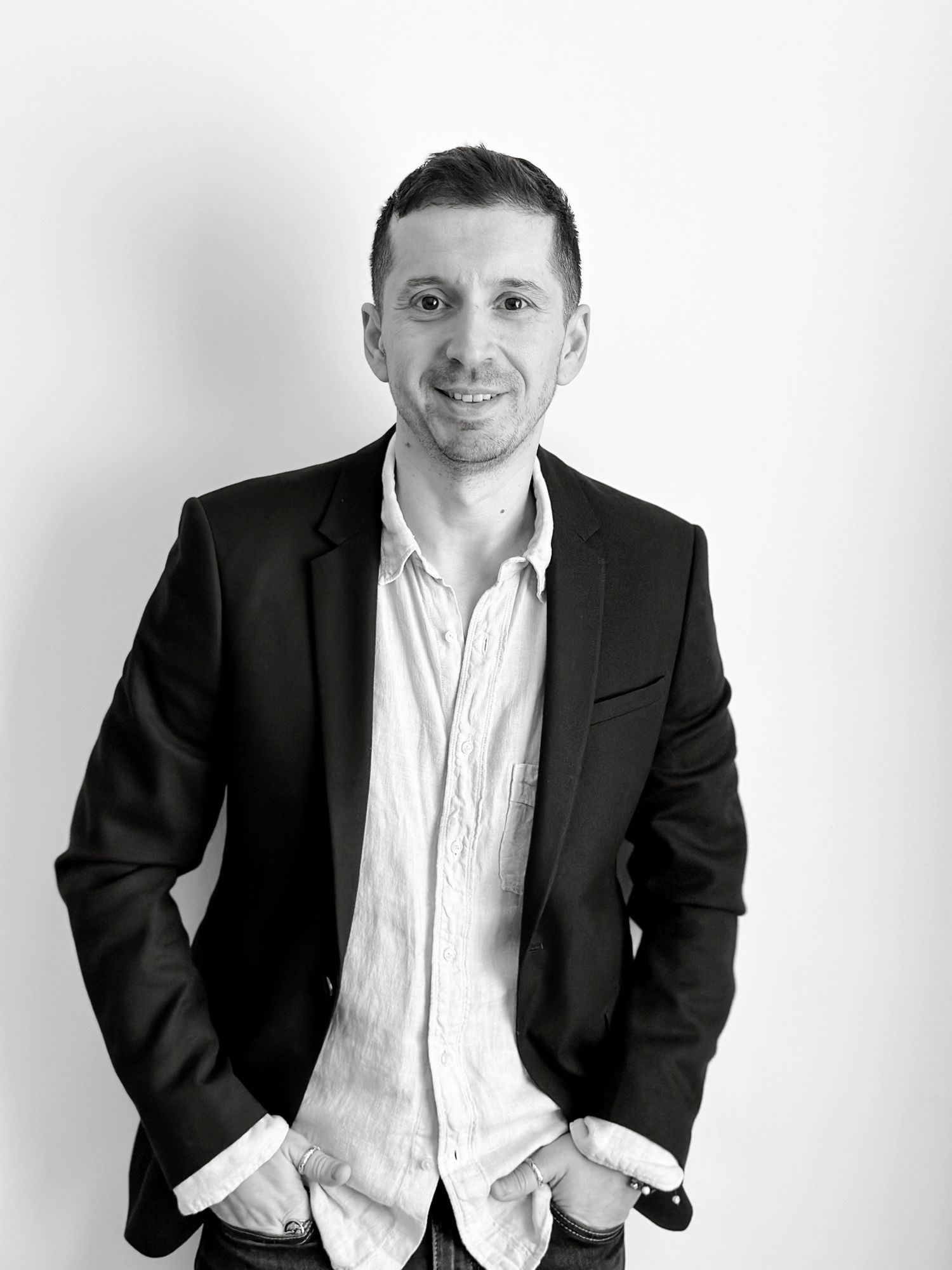 A smiling man in a black blazer and white shirt poses confidently in a professional black and white portrait photo.