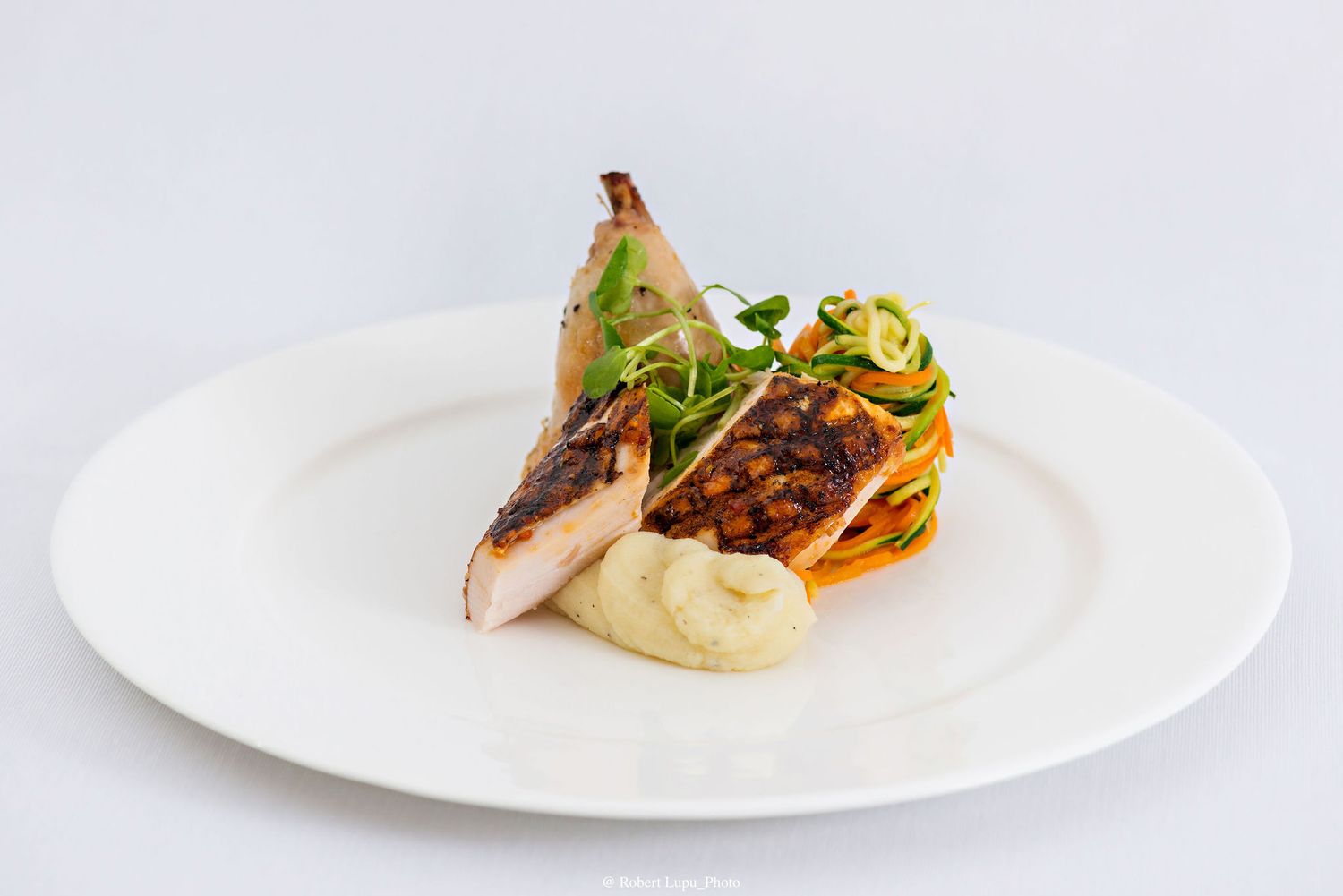 Elegant plated blackened fish fillet with creamy puree, zucchini noodles, and microgreens on a white ceramic plate.