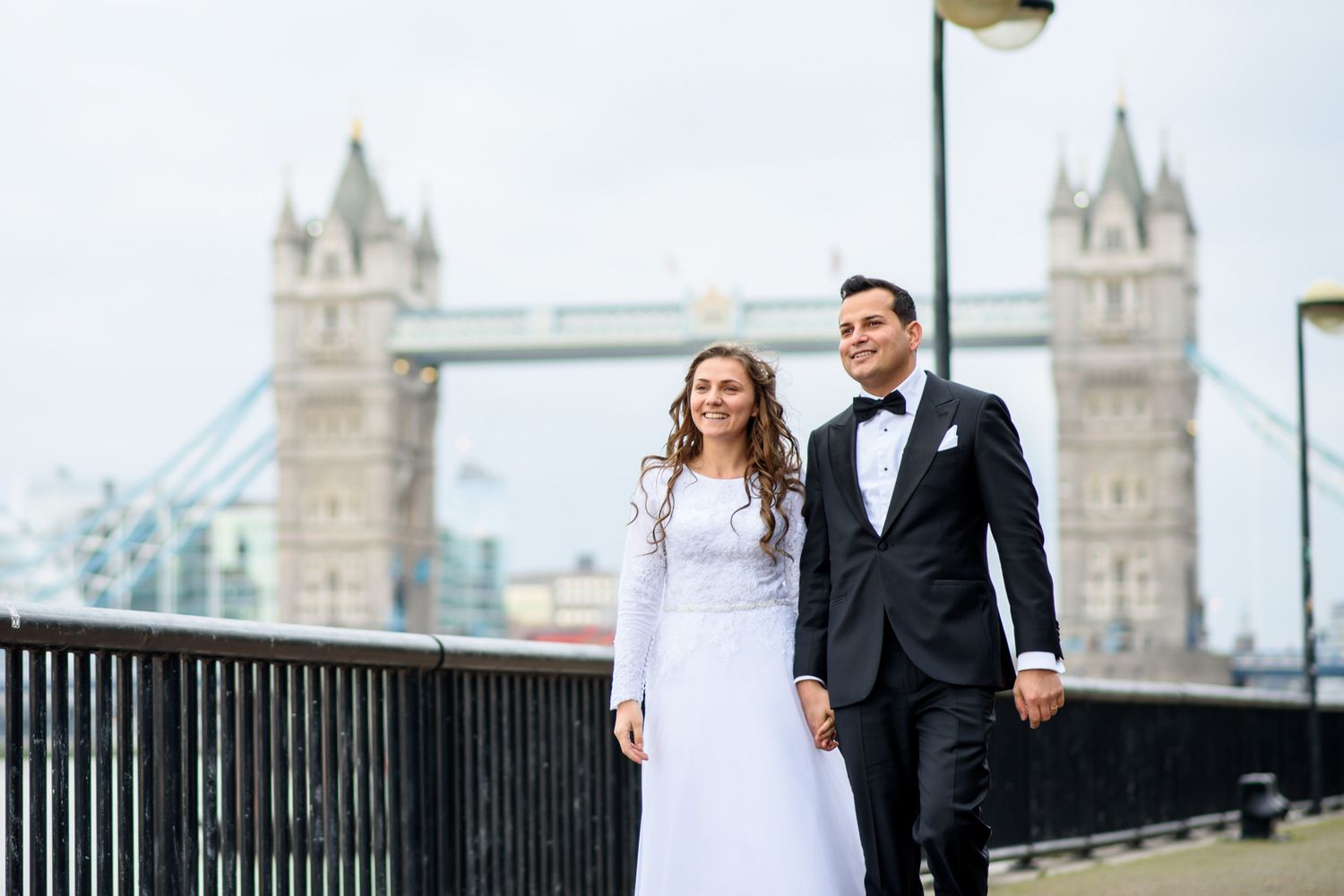 Newlywed couple in wedding attire holding hands with Tower Bridge London in the background.