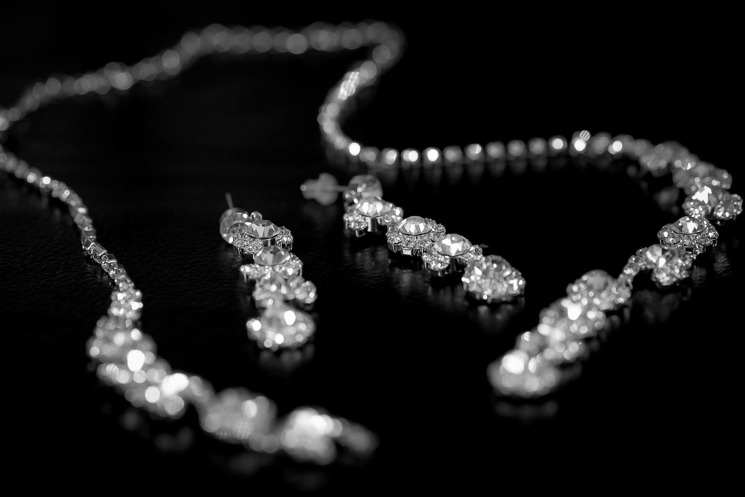 Sparkling diamond necklace and earring jewelry set displayed on a dark reflective surface.