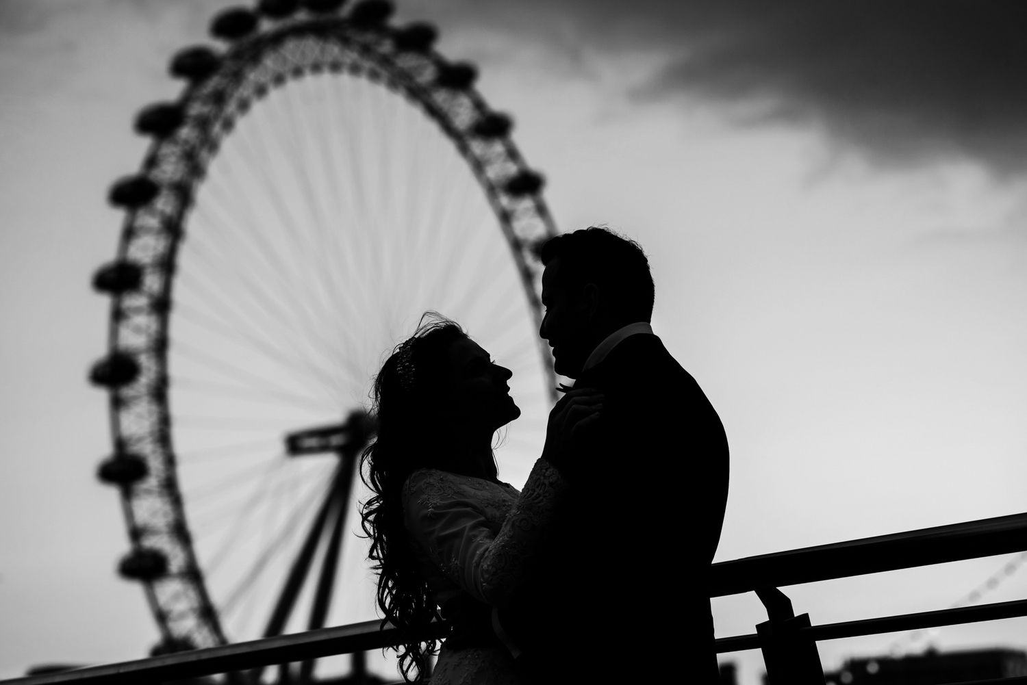 Romantic couple silhouette against London Eye ferris wheel at dusk in black and white photography.
