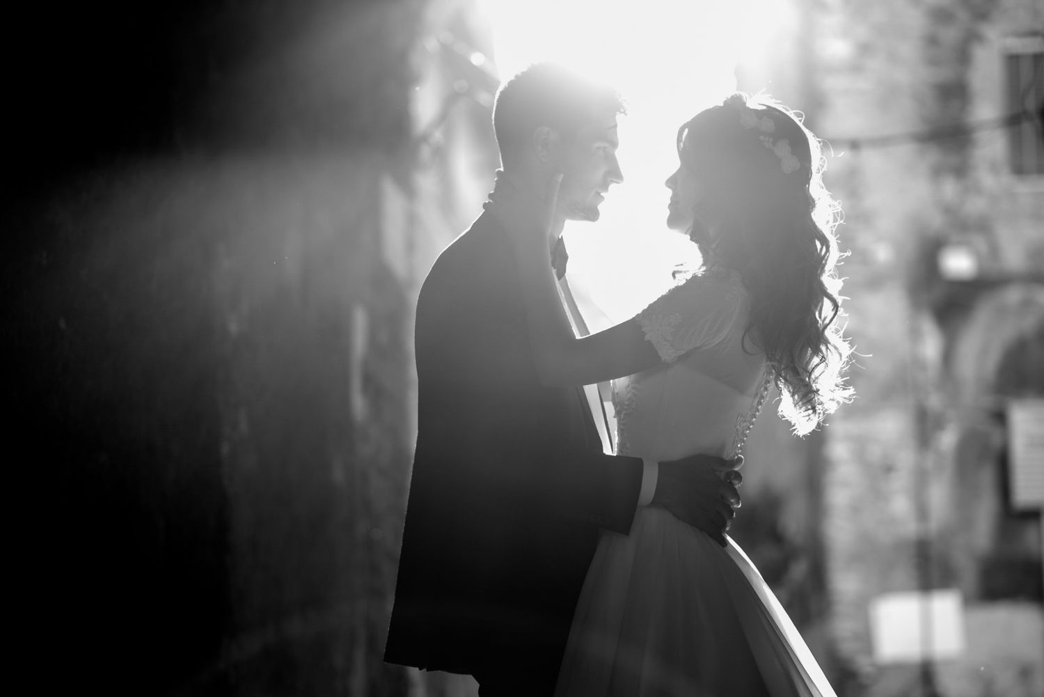 Romantic black and white silhouette of bride and groom facing each other in soft backlight.