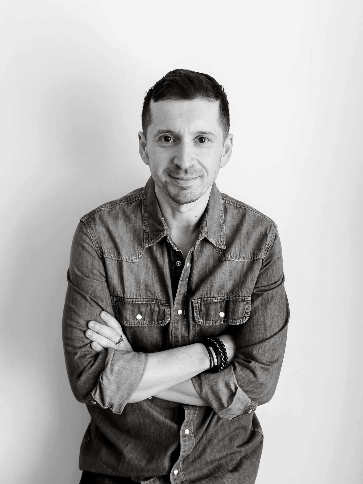 Black and white portrait of a smiling man with crossed arms wearing a denim shirt.
