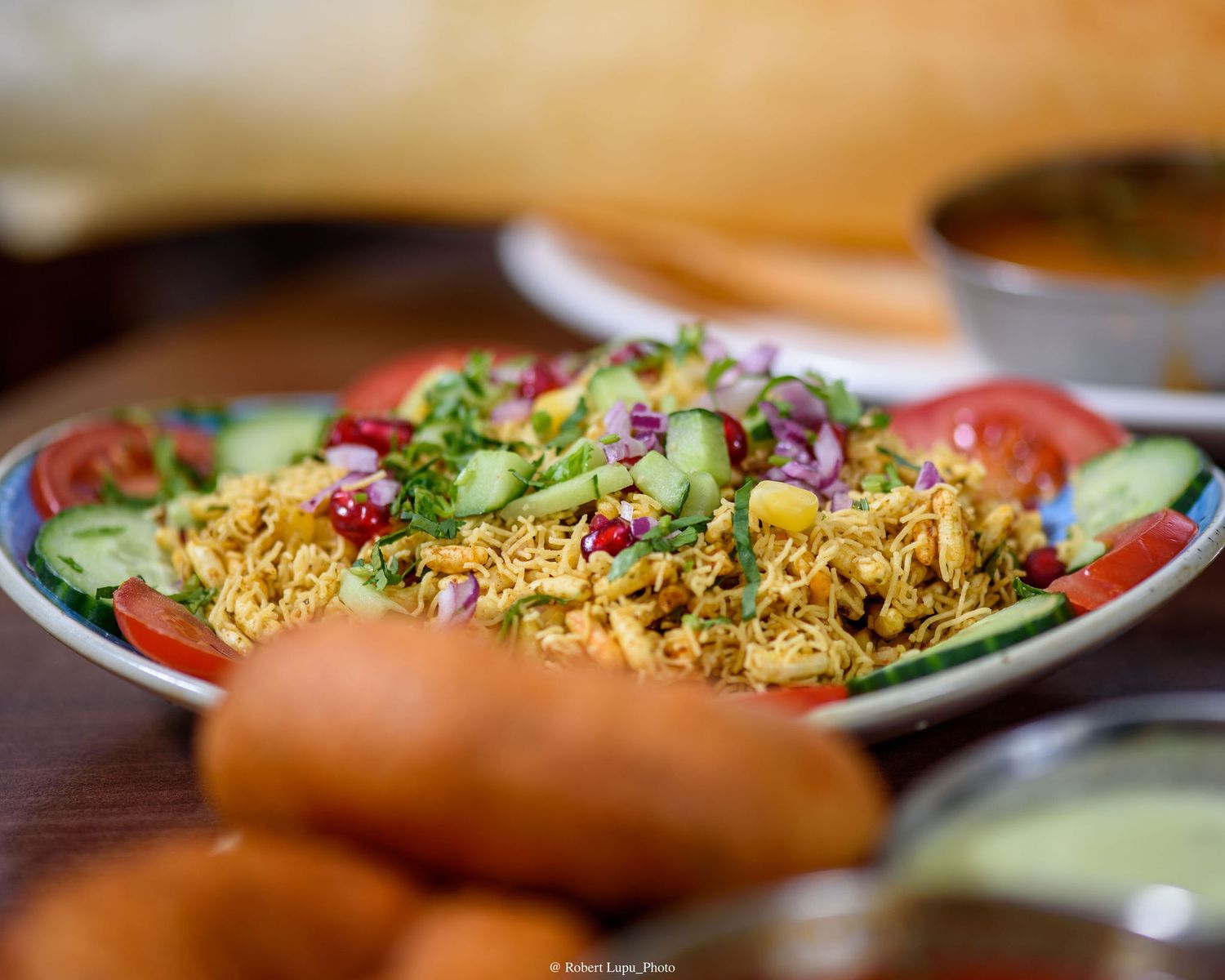 Colorful Indian chaat dish with crispy sev, fresh cucumber, tomatoes, and herbs served on a decorative plate.