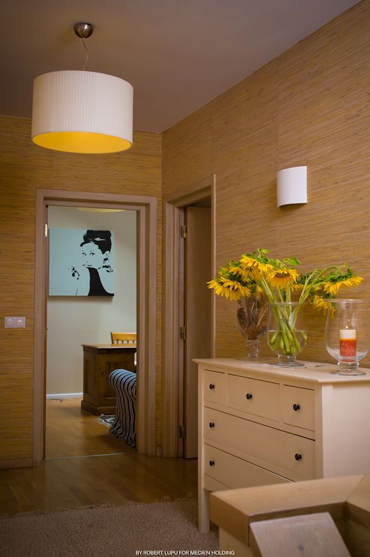 Cozy hallway with grasscloth walls, white drum pendant light, sunflowers on dresser, and Audrey Hepburn art in background.
