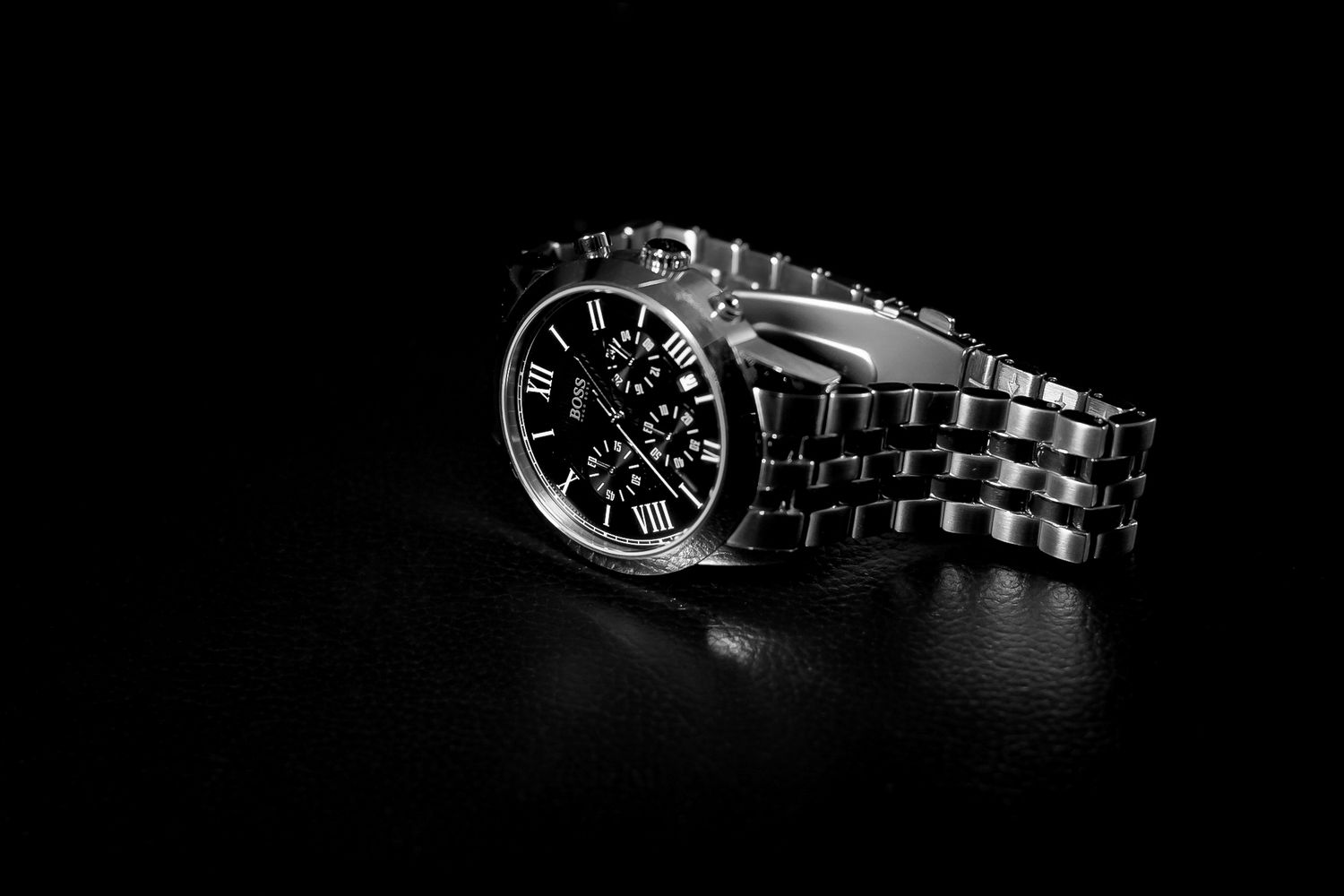 Elegant silver chronograph wristwatch with black dial and Roman numerals on dark reflective surface.