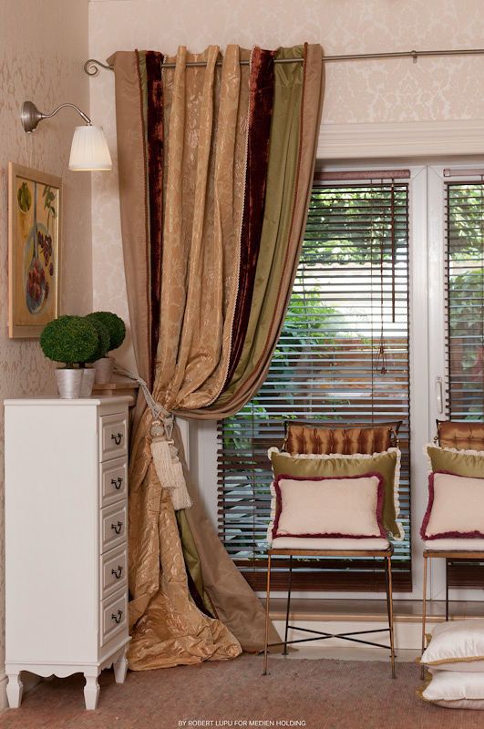Elegant multi-colored curtains in gold, burgundy, and green tied back beside a window with wooden blinds and a metal chair.