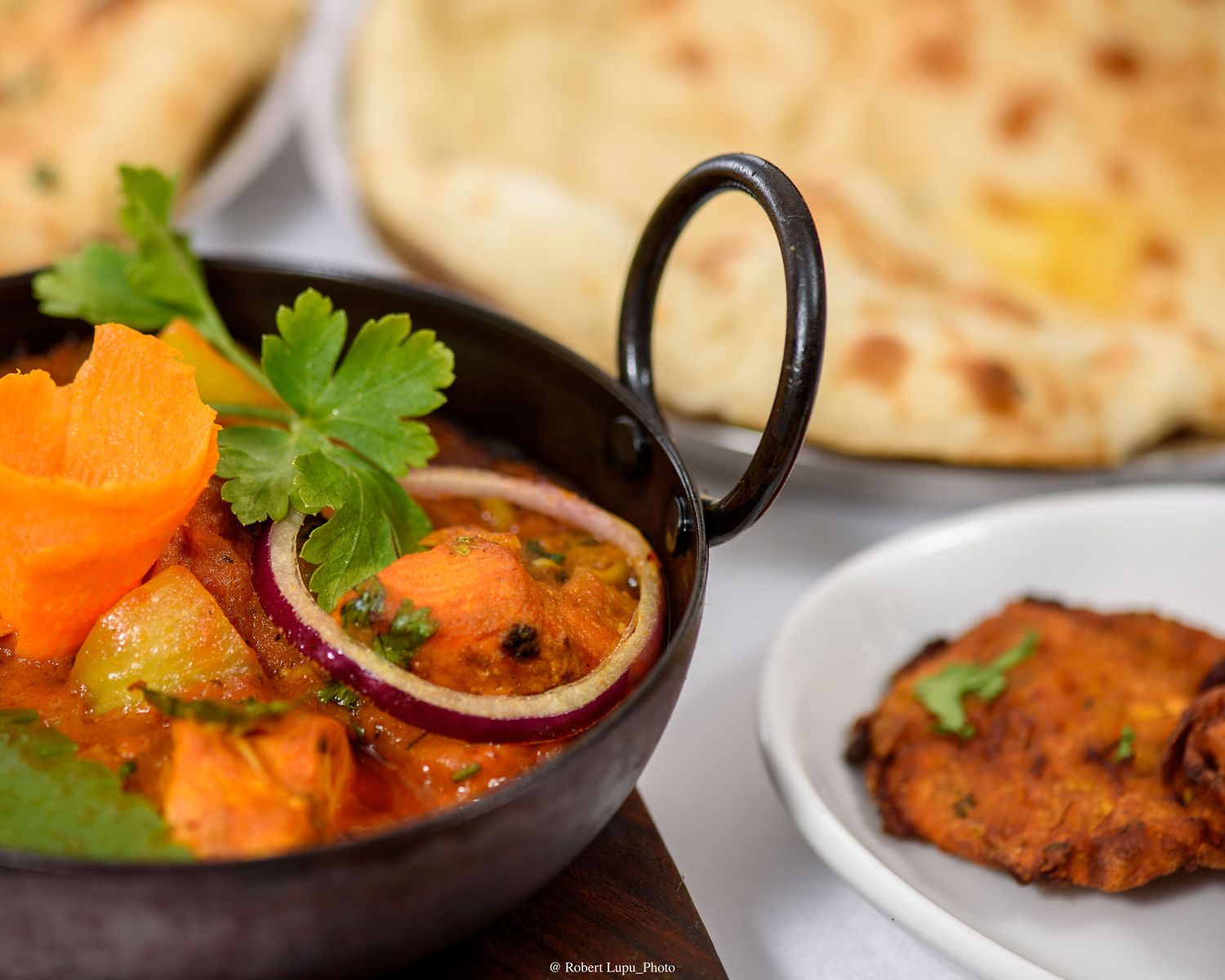 Vibrant Indian vegetable curry served in a traditional karahi with naan bread and spiced fritter.