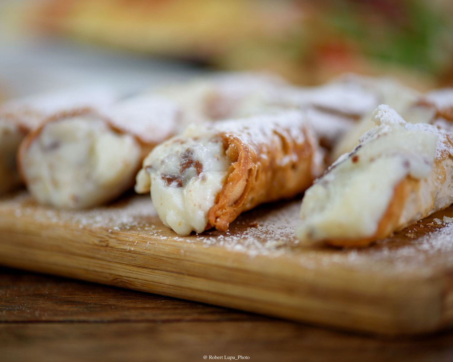Freshly made Sicilian cannoli dusted with powdered sugar on a wooden board, filled with creamy ricotta.