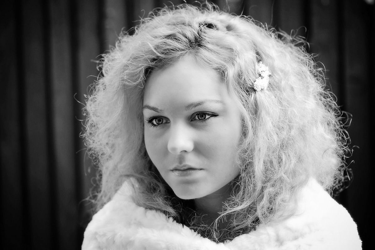 Curly blonde woman with flower hair accessory in white fur wrap, black and white close-up portrait.