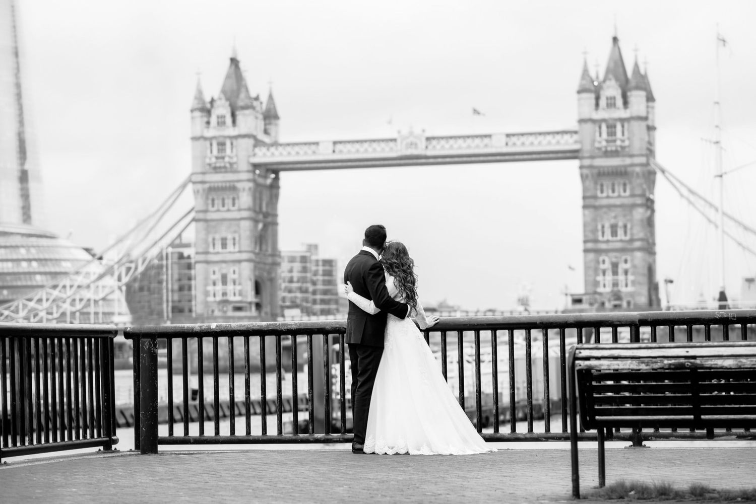 Bride and groom embrace before Tower Bridge London in a romantic black and white wedding portrait.